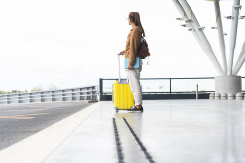 Junge Frau mit Gepäck auf Rädern auf dem Flughafen - JAQF00790