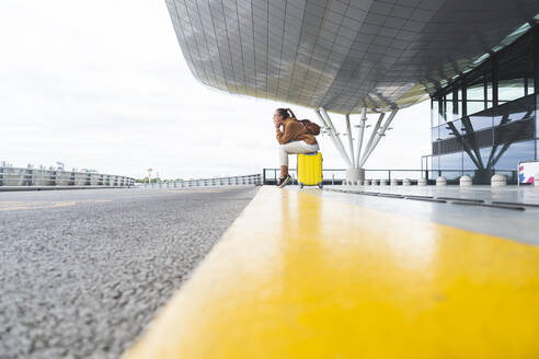 Junge Frau, die auf ihrem Gepäck sitzt und am Flughafen wartet - JAQF00796