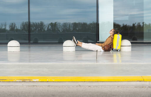 Woman with legs crossed at ankle leaning on luggage at airport - JAQF00800