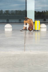 Junge Frau in Fötusstellung mit Gepäck auf dem Flughafen sitzend - JAQF00802