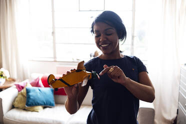 Lächelnde Frau spielt mit einem Spielzeug-Hubschrauber im Wohnzimmer - ASGF01547