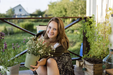 Lächelnde Frau mit Blumentopf in der Nähe von Pflanzen sitzend - LLUF00094