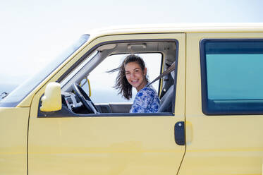 Glückliche erwachsene Frau im gelben Wohnmobil sitzend an einem sonnigen Tag - PGF00815