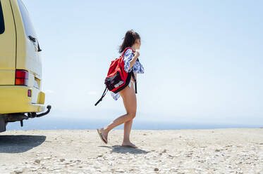Mittlere erwachsene Frau, die einen Rucksack trägt, während sie im Sommer am Strand spazieren geht - PGF00819