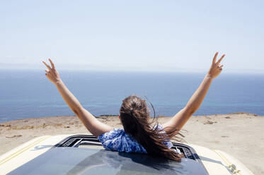 Carefree woman gesturing peace sign through sunroof of van during sunny day - PGF00823