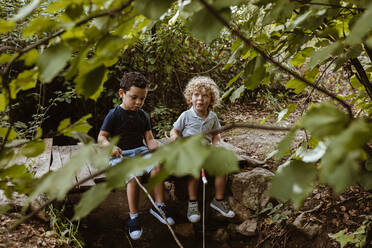 Junge spricht mit männlichem Freund auf einem Steg im Wald sitzend - MRRF01527