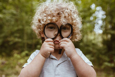 Sad boy holding magnifying glass over face - MRRF01537