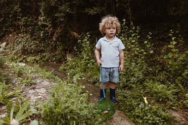Junge mit Fischernetz schaut weg, während er inmitten von Pflanzen steht - MRRF01559