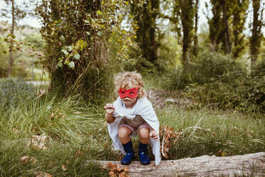 Niedlicher blonder Junge mit Umhang und Maske spielt im Wald - MRRF01565