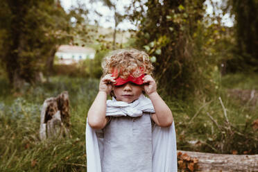 Boy with blond curly hair removing mask in forest - MRRF01568