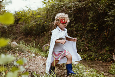 Boy wearing cape walking in forest - MRRF01569