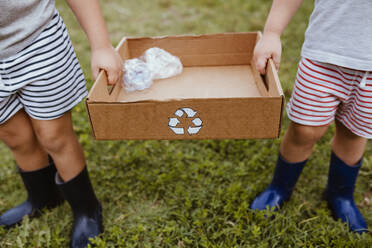 Jungen sammeln Plastik in einer Pappschachtel mit Recycling-Symbol - MRRF01580