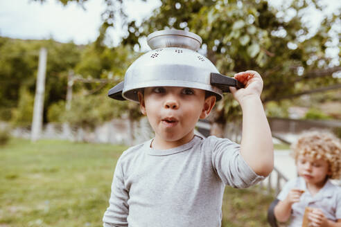 Playful boy wearing colander while playing on meadow - MRRF01591
