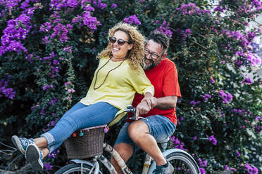 Glücklicher reifer Mann auf dem Fahrrad mit Freundin auf dem Korb sitzend im Park - SIPF02408