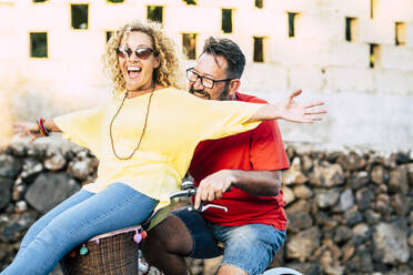 Happy man cycling with cheerful mature woman sitting on bicycle basket - SIPF02409