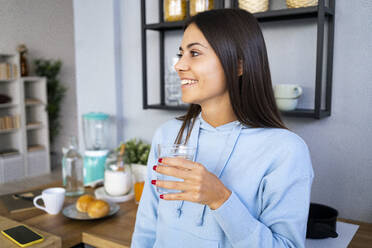 Lächelnde junge Frau hält ein Glas Wasser zu Hause - GIOF13578