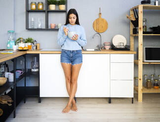 Woman having food while leaning on kitchen counter - GIOF13588