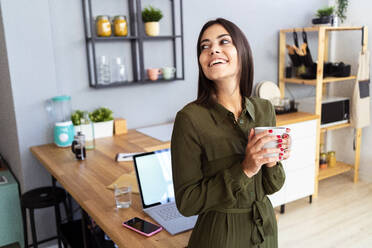 Glückliche Freiberuflerin hält Kaffeetasse zu Hause - GIOF13624