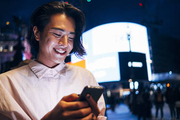 Happy man text messaging through smart phone in city at night - AMWF00012