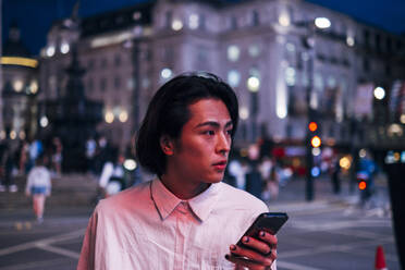 Handsome man with black hair holding mobile phone in city - AMWF00013