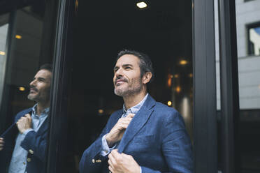 Smiling businessman at doorway of hotel - JCCMF03979