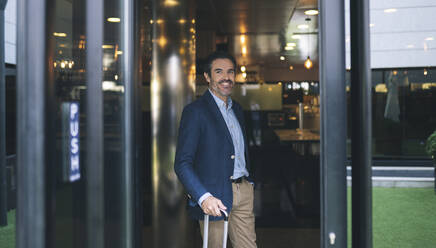 Smiling male professional with suitcase in hotel - JCCMF03980