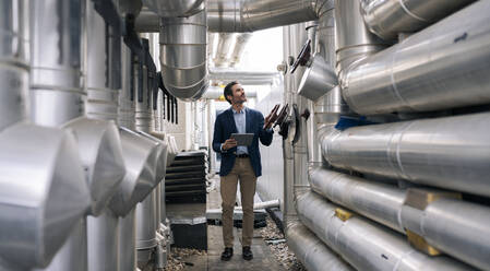 Businessman with digital tablet examining machinery at industry - JCCMF04006