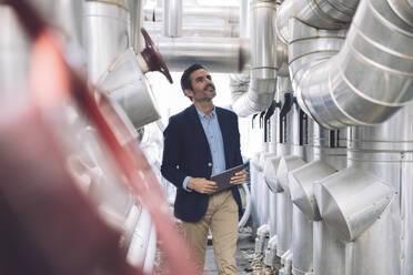 Smiling businessman looking at machinery in factory - JCCMF04011