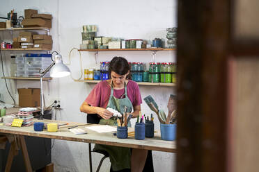 Female craftsperson making concrete design while sitting at workbench - VEGF05032