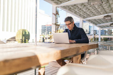 Junger Mann in trendigem Outfit beim Surfen auf dem Netbook, während er auf der Straße an einem Projekt arbeitet - ADSF30405