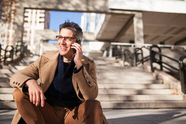 Stilvoller junger Mann mit Brille und Freizeitkleidung sitzt auf einer Treppe - ADSF30412