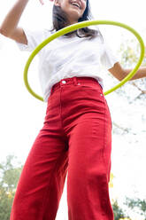 Von unten der Ernte unerkennbar fröhlichen weiblichen Teenager in roten Jeans wirbelnden Hula-Hoop-Reifen während der Freizeit im Park - ADSF30420