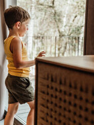 Gelassenes kleines Kind, das in der Nähe des Fensters in einem Häuschen steht und in Gedanken wegschaut - ADSF30437