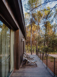 Zeitgenössisches Ferienhaus mit hölzernem Äußeren und geräumiger Terrasse in den Wäldern am Sommerabend - ADSF30448