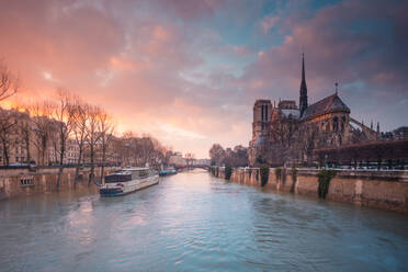 Touristenschiff schwimmt auf dem kräuselnden Wasser der Seine vorbei an der mittelalterlichen katholischen Kathedrale Notre Dame de Paris bei Sonnenuntergang - ADSF30457