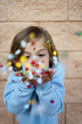 Girl blowing colorful confetti in front of wall - RCPF01297