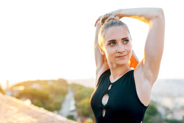 Eine fitte Frau in Sportkleidung streckt ihre Arme während einer Yogaübung auf dem Dach eines Gebäudes bei Sonnenuntergang - ADSF30485