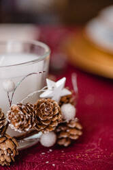 Kerze in einem mit Zapfen und Sternen verzierten Glashalter auf einem Tisch, der zur Weihnachtsfeier dient - ADSF30506