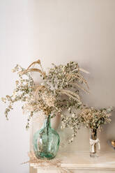 Glasvasen mit getrockneten Pflanzen und mit Blättern bedeckten Zweigen zur Dekoration des Wohnzimmers - ADSF30507
