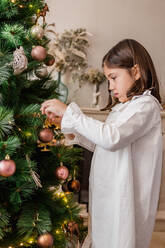 Seitenansicht der Ernte konzentriert Mädchen schmücken Weihnachtsbaum Zweige bei der Vorbereitung zu Hause für Urlaub Feier - ADSF30511