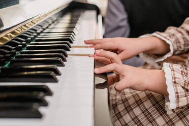 Crop unerkennbar Kind in karierten Kleid spielen Klavier während der Freizeit zu Hause auf unscharfen Hintergrund - ADSF30531