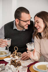 Crop fröhliches Paar mit Gläsern von alkoholischen Getränken interagieren, während lachend am Tisch mit Sahne Suppen während Neujahr Urlaub - ADSF30533