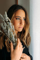 Portrait of gorgeous teen girl at home holding a branch of lavender and looking away - ADSF30538