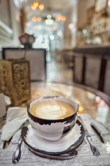 Keramiktasse mit aromatischem Kaffee und Latte Art auf einem Tisch mit Servietten und blühender Rose in einer Cafeteria - ADSF30543