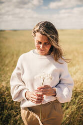 Lächelnde blonde Frau betrachtet eine Blume an einem sonnigen Tag - GRCF00921