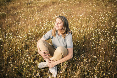 Lächelnde reife Frau mit blondem Haar sitzt auf einem Feld - GRCF00955