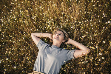 Carefree woman with hands behind head lying amidst plants during weekend - GRCF00956