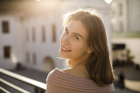 Lächelnde junge Frau auf dem Dach an einem sonnigen Tag - LLUF00108