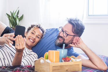 Lächelndes Paar teilt sich ein Handy auf dem Bett zu Hause - SIPF02423