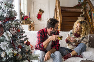 Smiling woman having coffee with man while sitting on sofa at home during Christmas - SIPF02424